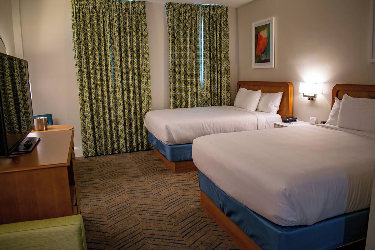 A hotel room with two beds, a desk with a telephone, and a painting on the wall.