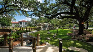 A landscaped garden with a wooden bridge, a small waterfall, and a white building in the background. - Centennial Plaza Resort Gulfport (Gulfport)