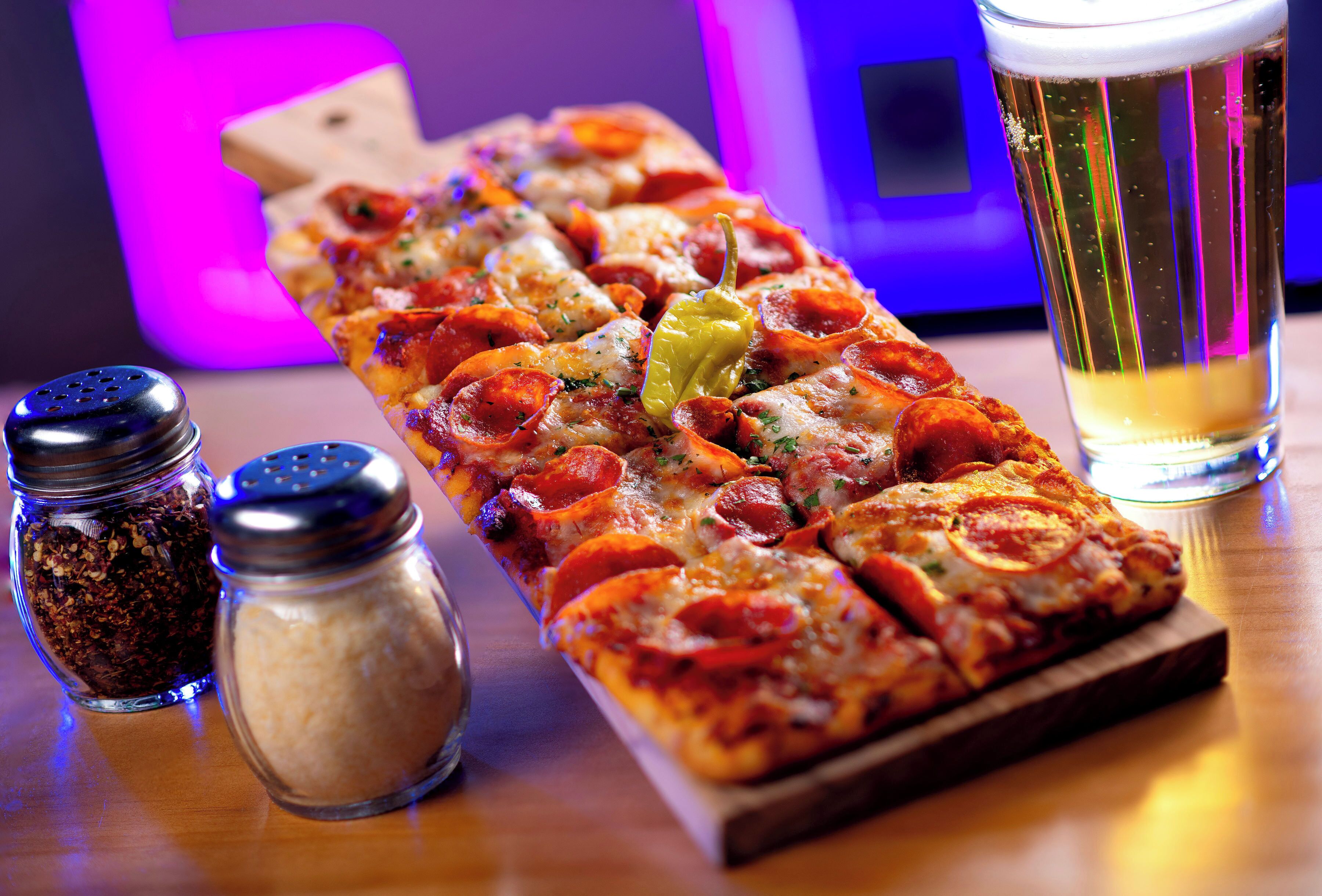 A pepperoni pizza on a wooden board with two salt and pepper shakers beside it.