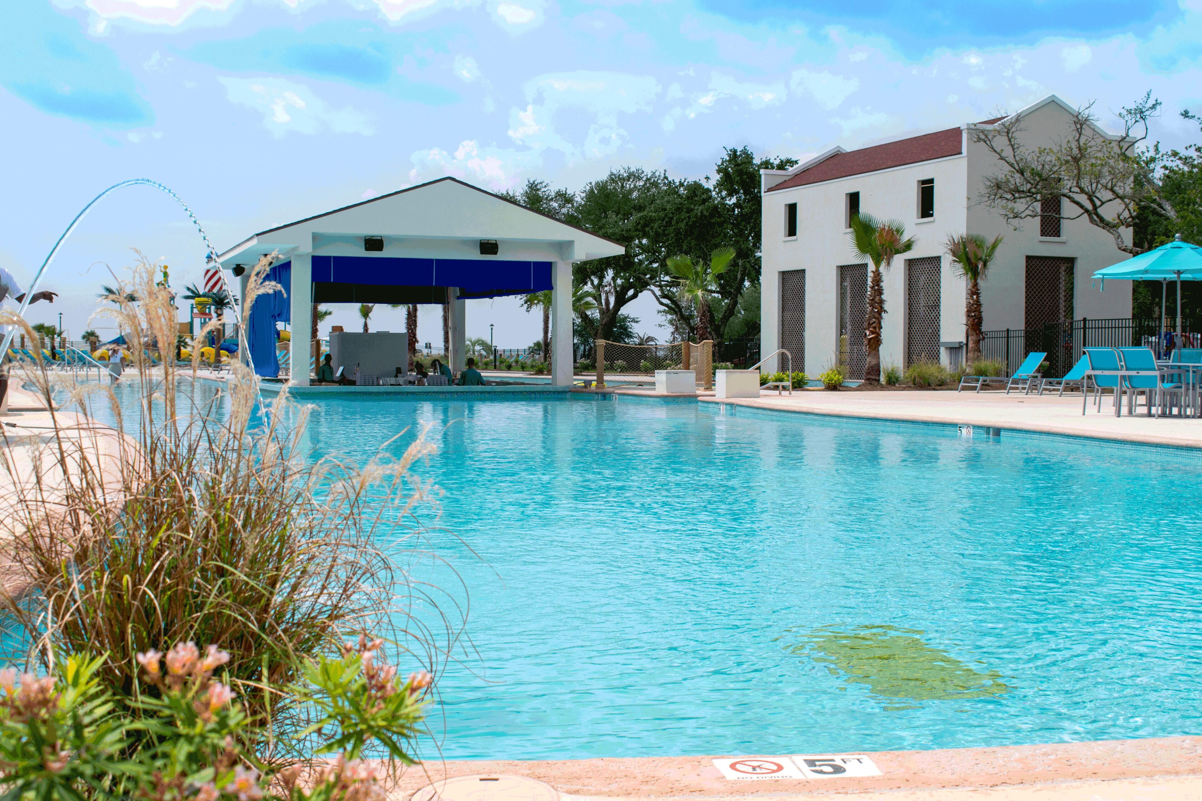 A swimming pool with a covered area, lounge chairs, and a building with a red roof.