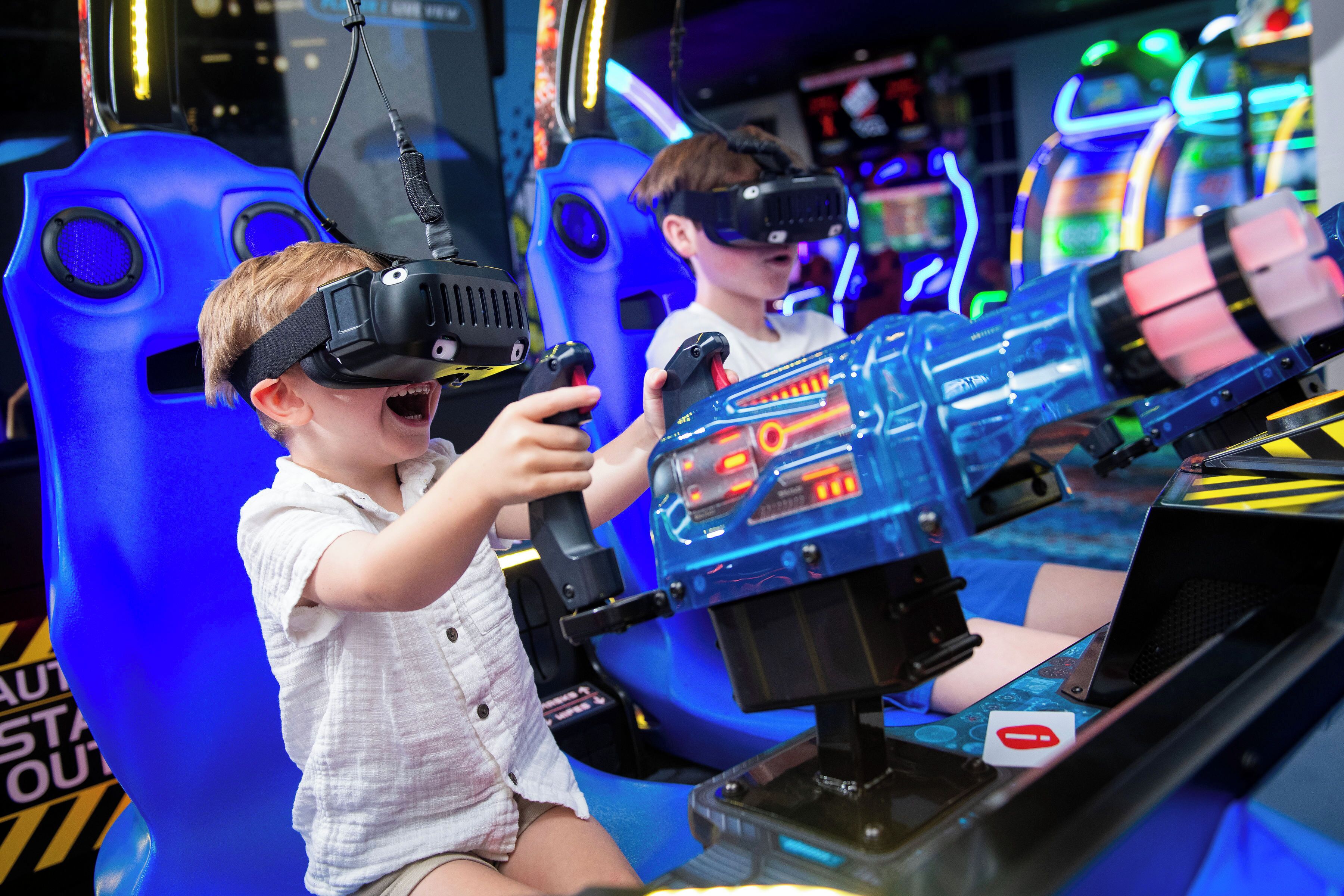 Un enfant portant un casque de réalité virtuelle dans un espace de jeux, avec des chaises bleues et des néons.