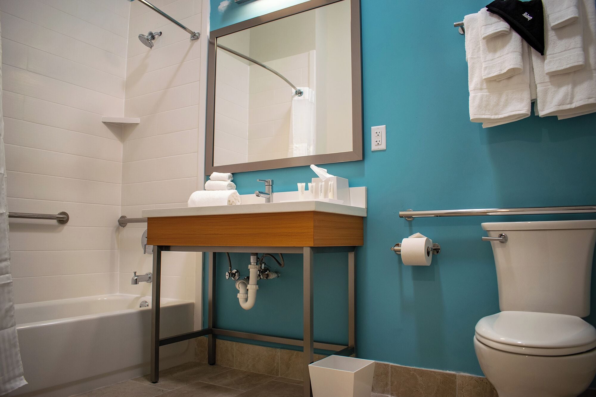 Un baño con bañera, lavamanos con artículos de aseo, inodoro y toallas colgadas en la pared.