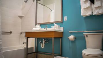 Un baño con bañera, lavamanos con artículos de aseo, inodoro y toallas colgadas en la pared.