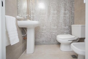 A bathroom with a white sink, toilet, and bidet. The walls have a patterned tile design. - H48 Venezuela Apartment (Córdoba)