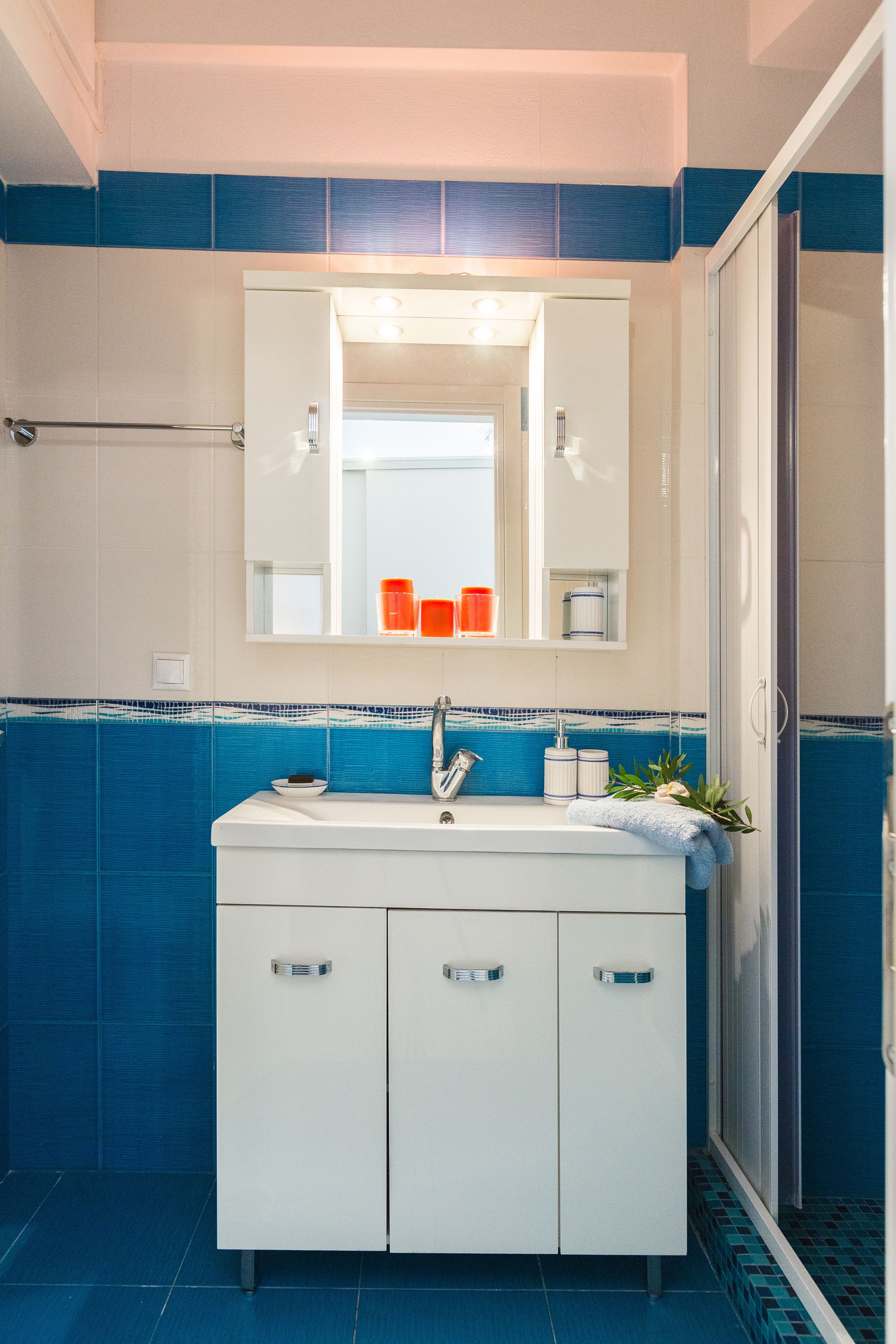 A bathroom with a white vanity, blue tiled walls, a mirror, and a shower area.