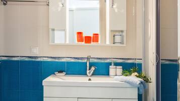 A bathroom with a white vanity, blue tiled walls, a mirror, and a shower area.