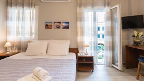 A hotel room with a bed, a desk, a TV, and a balcony with a view. - Casa Voula (Corfu)
