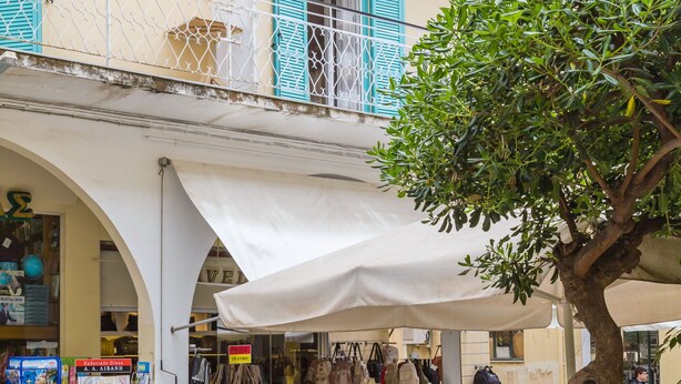 An outdoor café with tables and chairs, a signboard, and a shop with bags and accessories. - Casa Voula (Corfu)