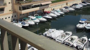 A marina with multiple boats docked, a large building with balconies, and a clear sky.