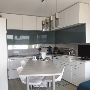 A modern kitchen with white cabinetry, a dining table with chairs, and pendant lights. - Overlooking the marina, close to the sea and town center, rated 3*. (Mandelieu-la-Napoule)