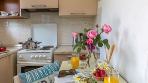 A kitchen with a stove, a table with a placemat, a vase with flowers, and a glass of orange juice. - Foxy Studio 2 (Corfu)