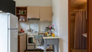 A compact kitchen with a refrigerator, stove, and a dining table with chairs. - Foxy Studio 2 (Corfu)