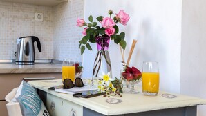 A kitchen counter with a kettle, a bowl of fruit, a vase with flowers, and two glasses of orange juice. - Foxy Studio 2 (Corfu)