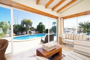 Un vaste salon doté d’une grande porte vitrée donnant sur une piscine, d’un canapé et d’une table basse en bois.