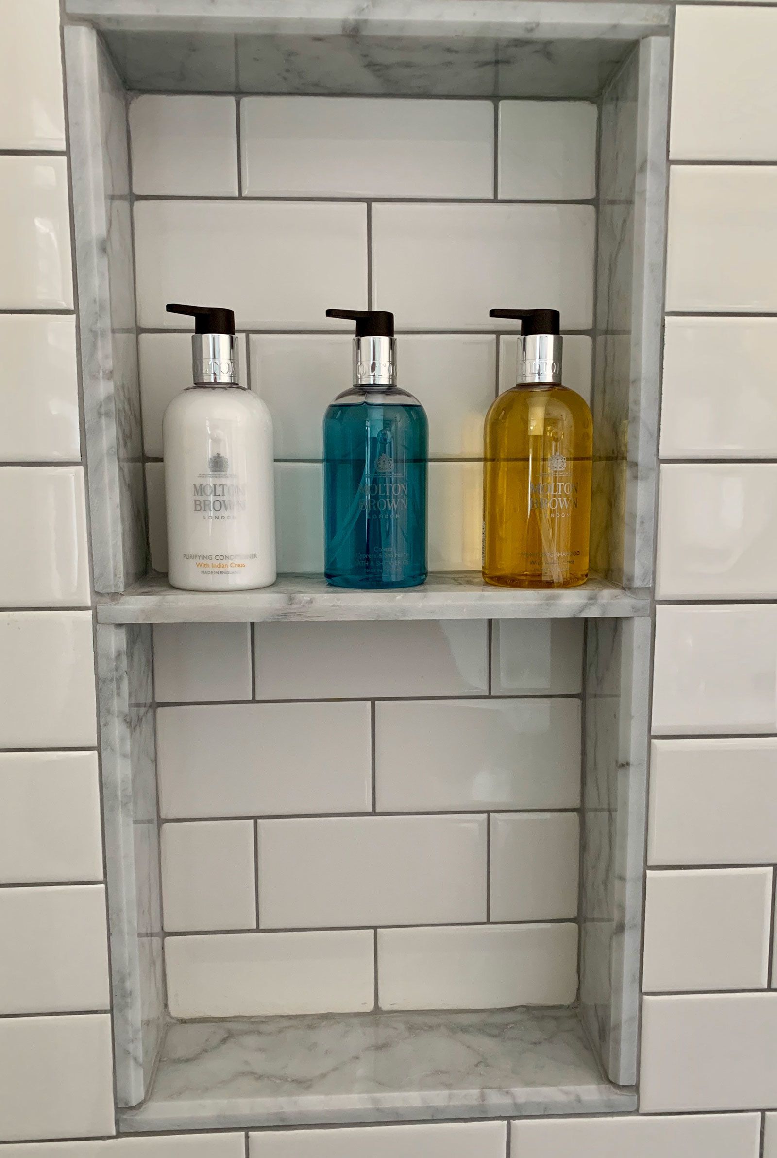 Une étagère de salle de bain avec trois bouteilles de savon liquide.