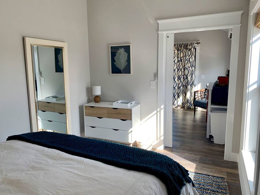 A bedroom with a bed, dresser, and a mirror. There is a door leading to another room with a patterned curtain.
