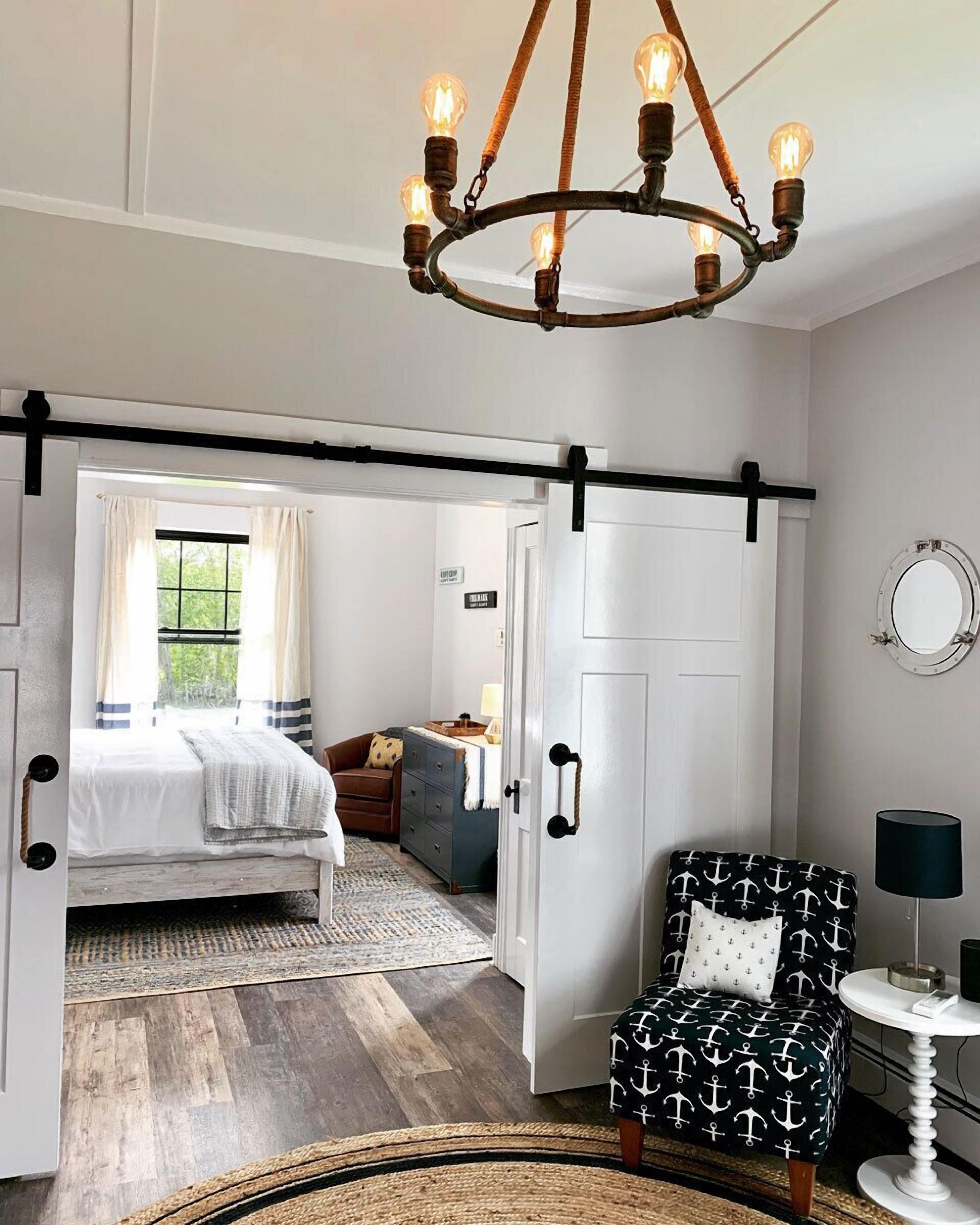 A bedroom with a bed, a chair, a dresser, a mirror, and a chandelier.
