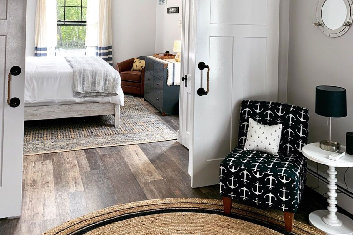 A bedroom with a bed, a chair, a dresser, a mirror, and a chandelier.
