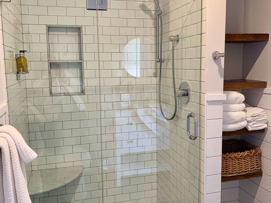 A glass-enclosed shower with white tiles, a handheld showerhead, and a handheld shower attachment.