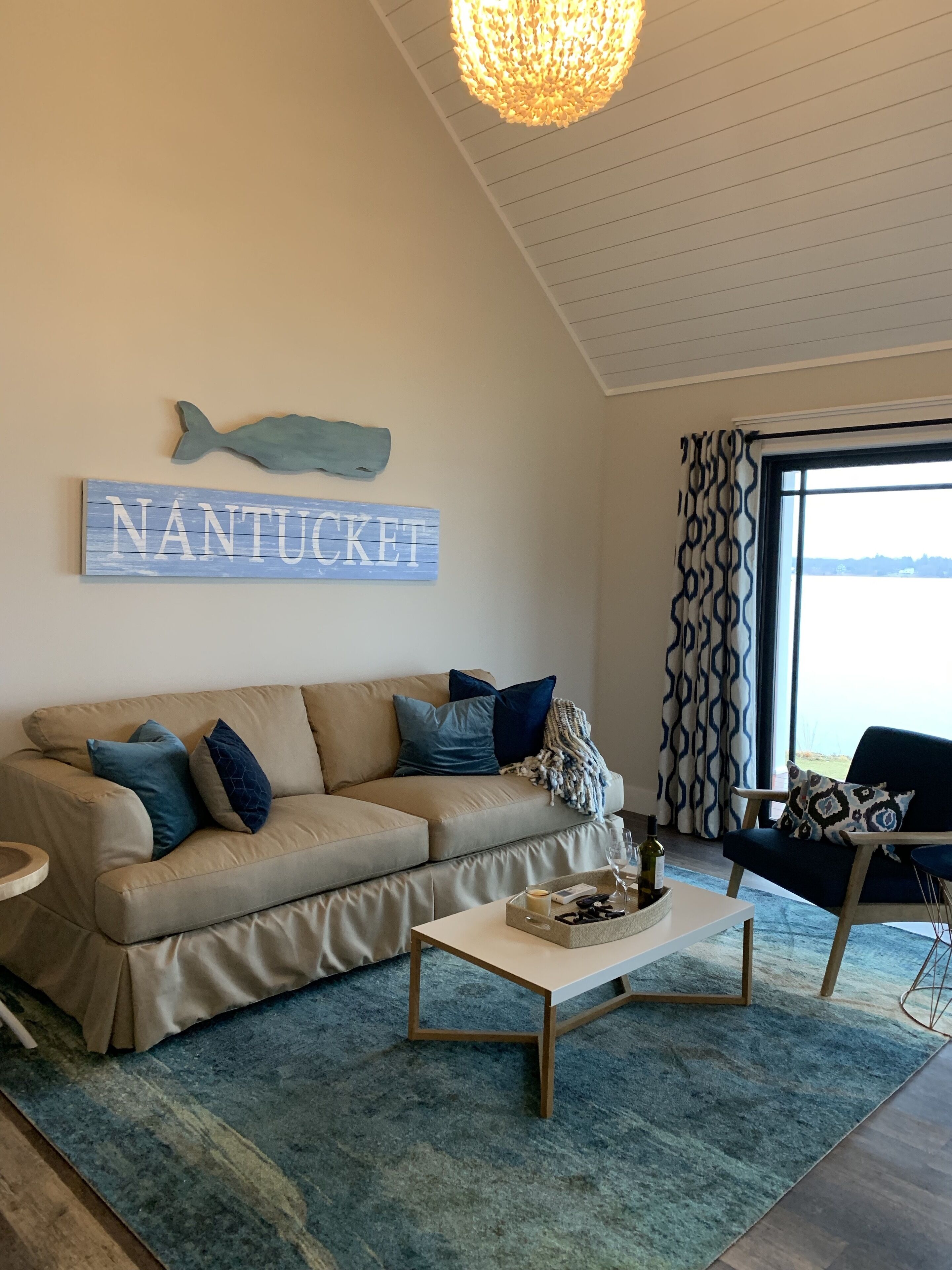 Una sala de estar con un sofá color beige, una mesa de centro y una pared azul decorada con un pez y la palabra "NANTUCKET".