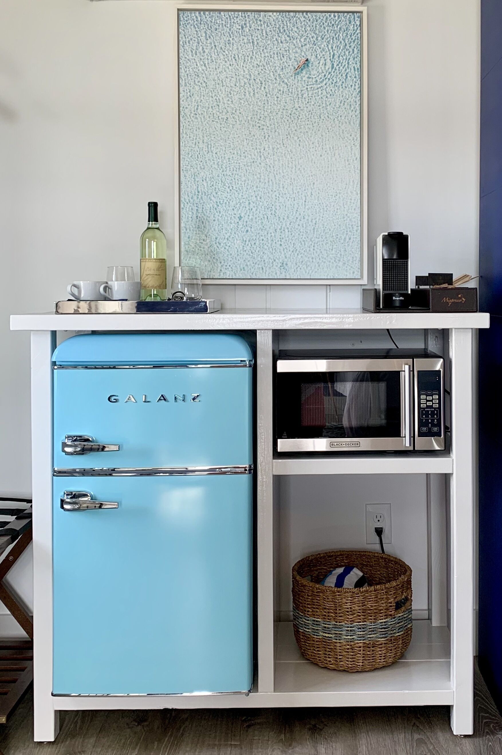 A blue Galanz refrigerator, a microwave, and a wicker basket on a white shelf.