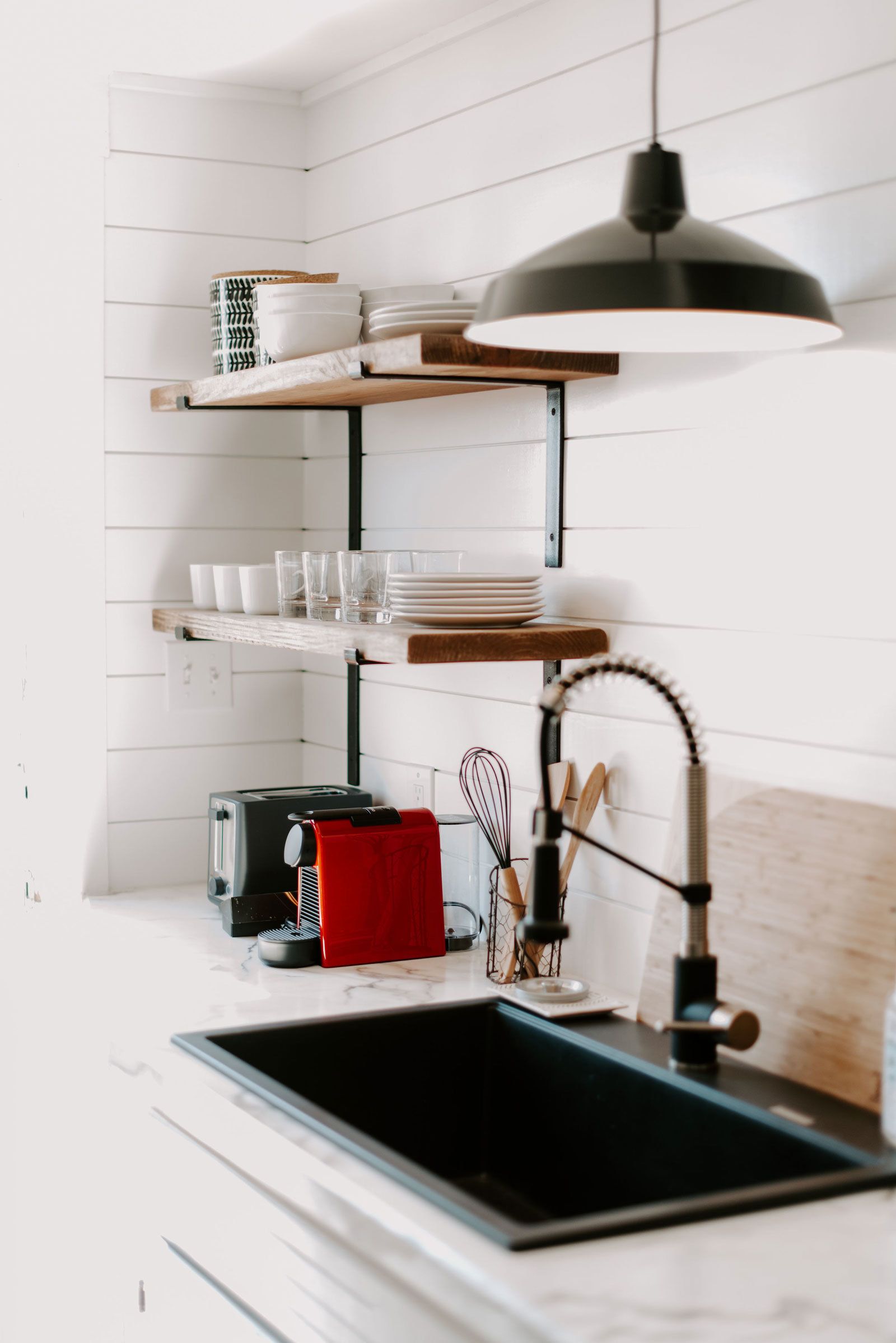 A modern kitchen with white cabinetry, a black sink, a red towel, and a black pendant light.