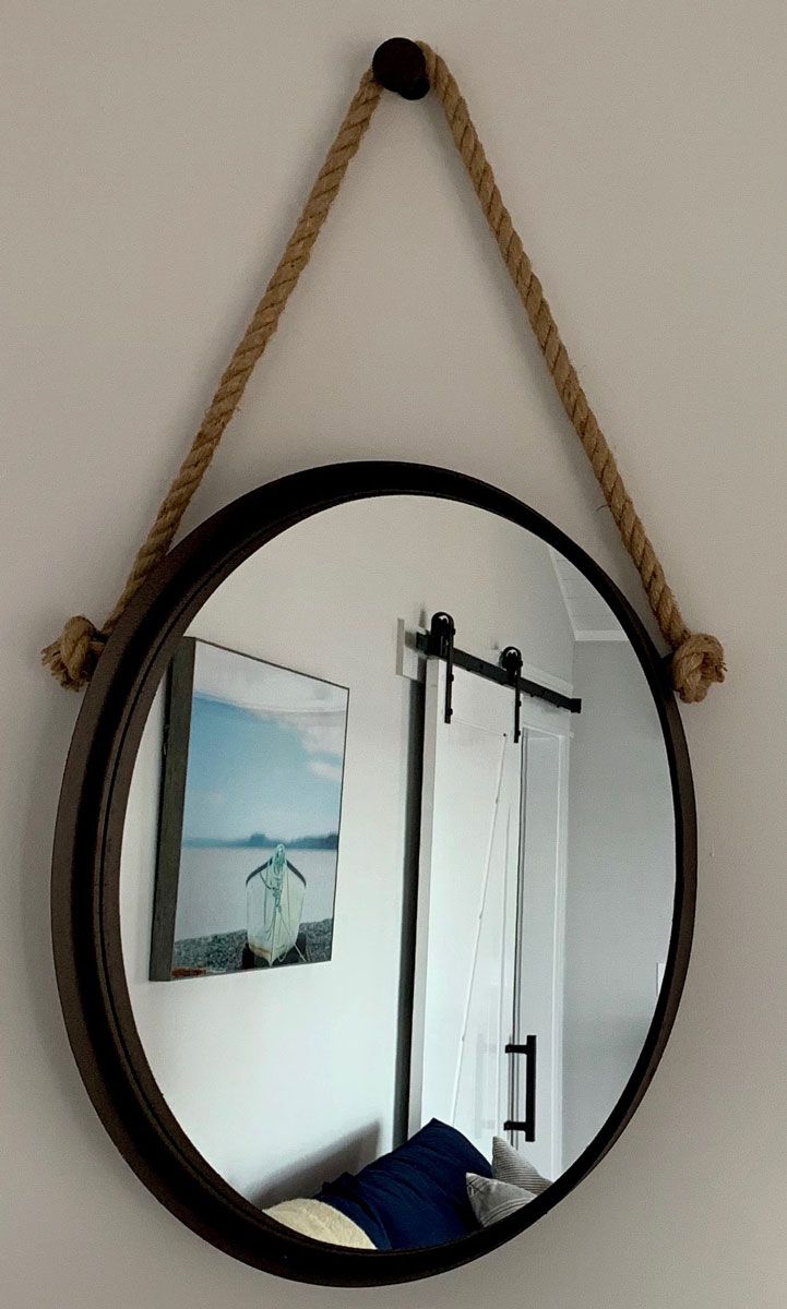 A round mirror with a rope handle, a bed with pillows, and a framed picture on the wall.