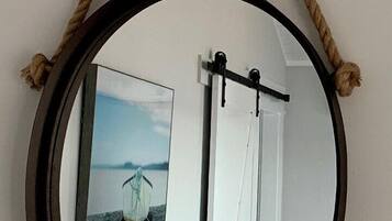 A round mirror with a rope handle, a bed with pillows, and a framed picture on the wall.