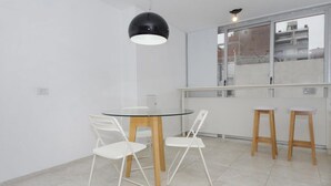 A modern dining area with a glass table, white chairs, and a black pendant light. - Velez Sarsfield Apartment AJC (Córdoba)