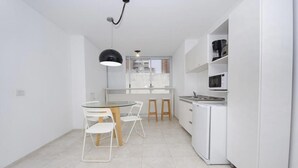 A compact kitchen with white cabinetry, a round dining table with chairs, a hanging pendant light, and a view through a window. - Velez Sarsfield Apartment AJC (Córdoba)