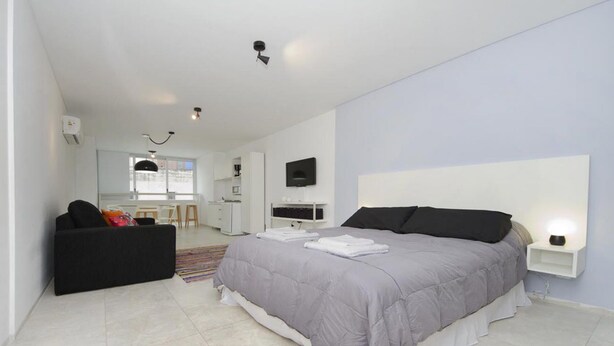 A modern bedroom with a large bed, a black sofa, a TV mounted on the wall, and a small bedside table. - Velez Sarsfield Apartment AJC (Córdoba)