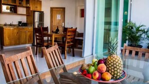 Una cocina moderna con armarios de madera, un refrigerador de acero inoxidable y un comedor con mesa y sillas de vidrio.