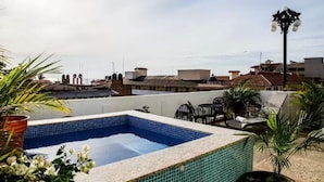 Una piscina en la azotea con borde de azulejos, rodeada de plantas en macetas y mobiliario exterior.