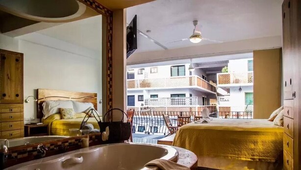 Una habitación de hotel con una bañera grande, una cama, un balcón con vistas a otros edificios y un ventilador de techo.