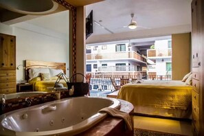 A hotel room with a large bathtub, a bed, a balcony with a view of other buildings, and a ceiling fan. - Hotel Andales on the Bay Suites (Puerto Vallarta)
