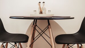 Et bord med hvid overflade og sorte kanter, hvilende på træben med et krydsformet design. To sorte stole er placeret på hver side af bordet.