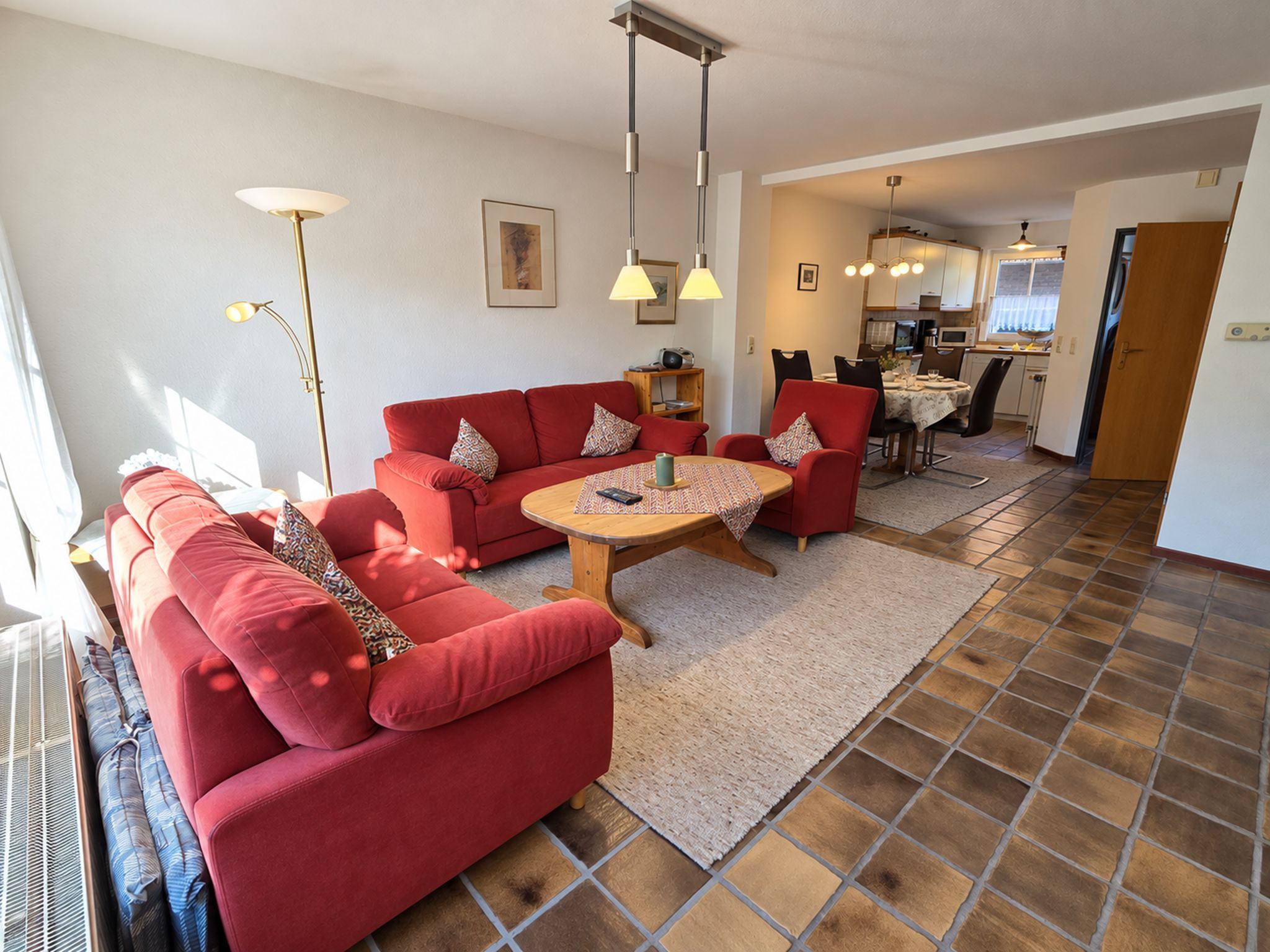 A living room with a red sofa set, a round coffee table, and a dining area with a kitchen in the background.