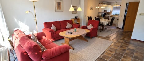 A living room with a red sofa set, a round coffee table, and a dining area with a kitchen in the background.