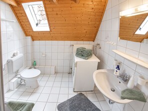 Baño pequeño y funcional con techo de madera, inodoro, lavadora y lavamanos.