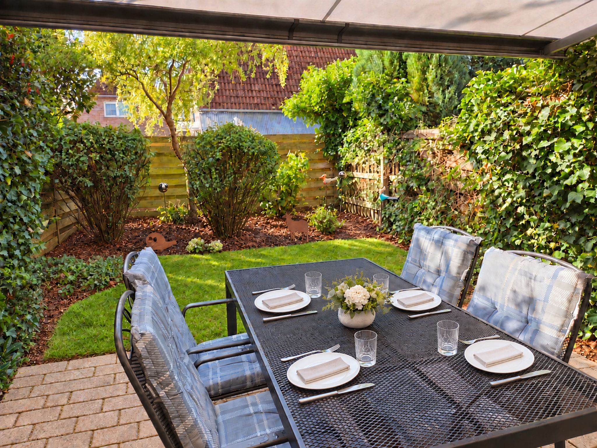 Een terras buiten, met een tafel gedekt voor twee personen, omgeven door groen en een houten omheining.