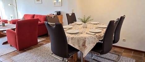 A dining area with a table set for four, surrounded by chairs, a red sofa, and a lamp in the background.