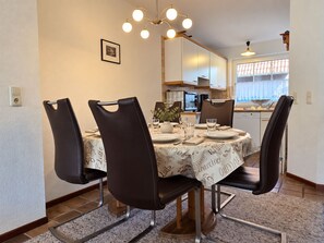 Un coin repas avec une table ronde, quatre chaises, un lustre et une cuisine en arrière-plan.
