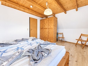 Un dormitorio con techo de madera, una cama con manta a rayas, un armario de madera y una silla de madera.