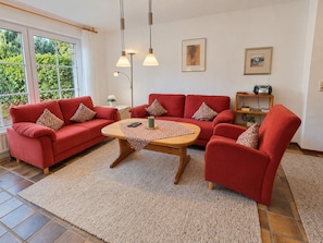 Una sala de estar con un sofá rojo, una mesa de centro de madera y un ventanal con vista a zonas verdes.