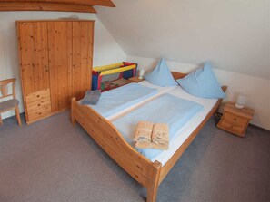 A bedroom with a wooden bed, two pillows, a nightstand, a wardrobe, and a chair. - Vacation home lighthouse, holiday apartment rental North Sea - vacation home lighthouse (Varel)