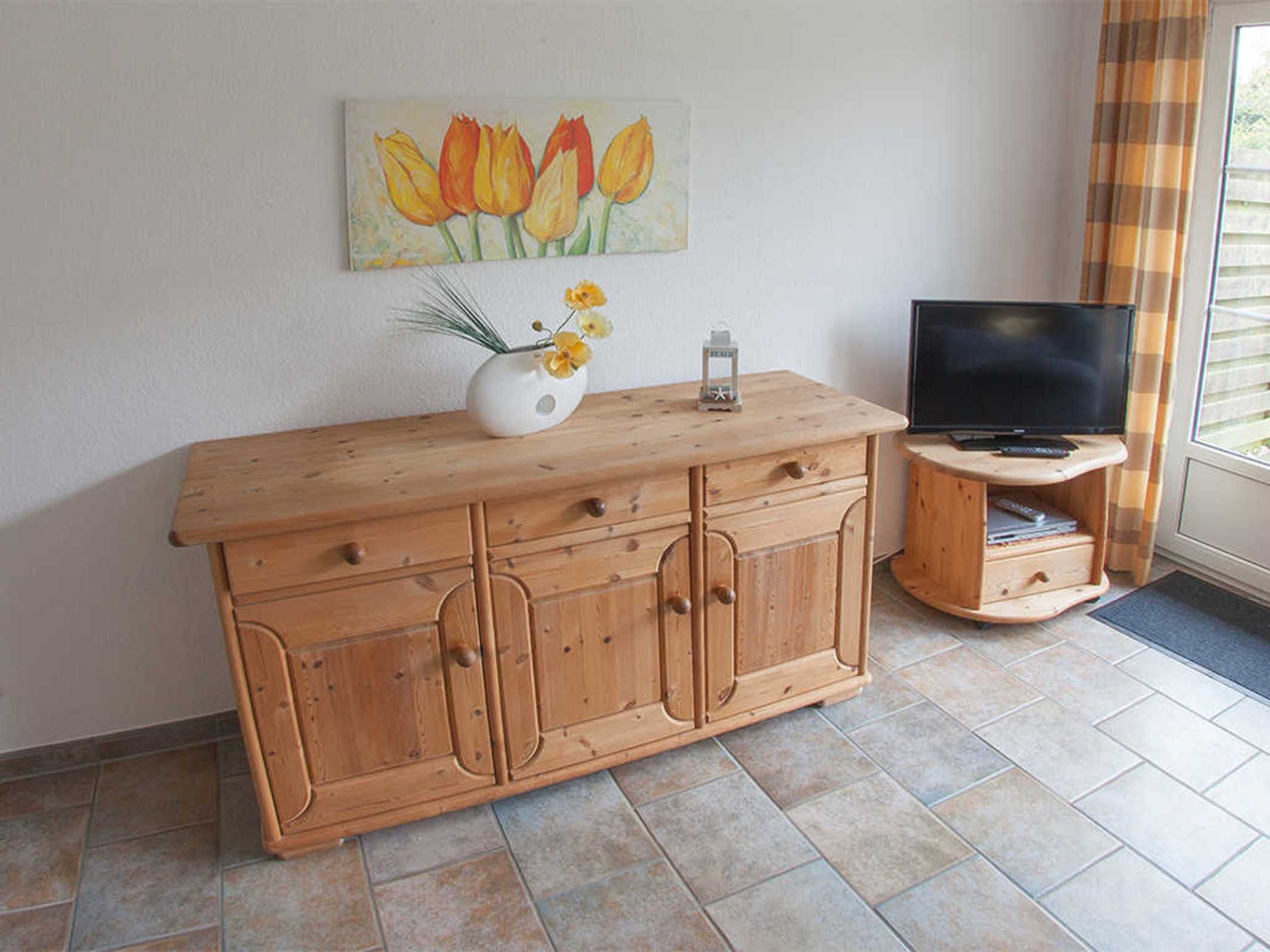 A wooden cabinet with drawers, a vase with flowers, and a painting of tulips on the wall.