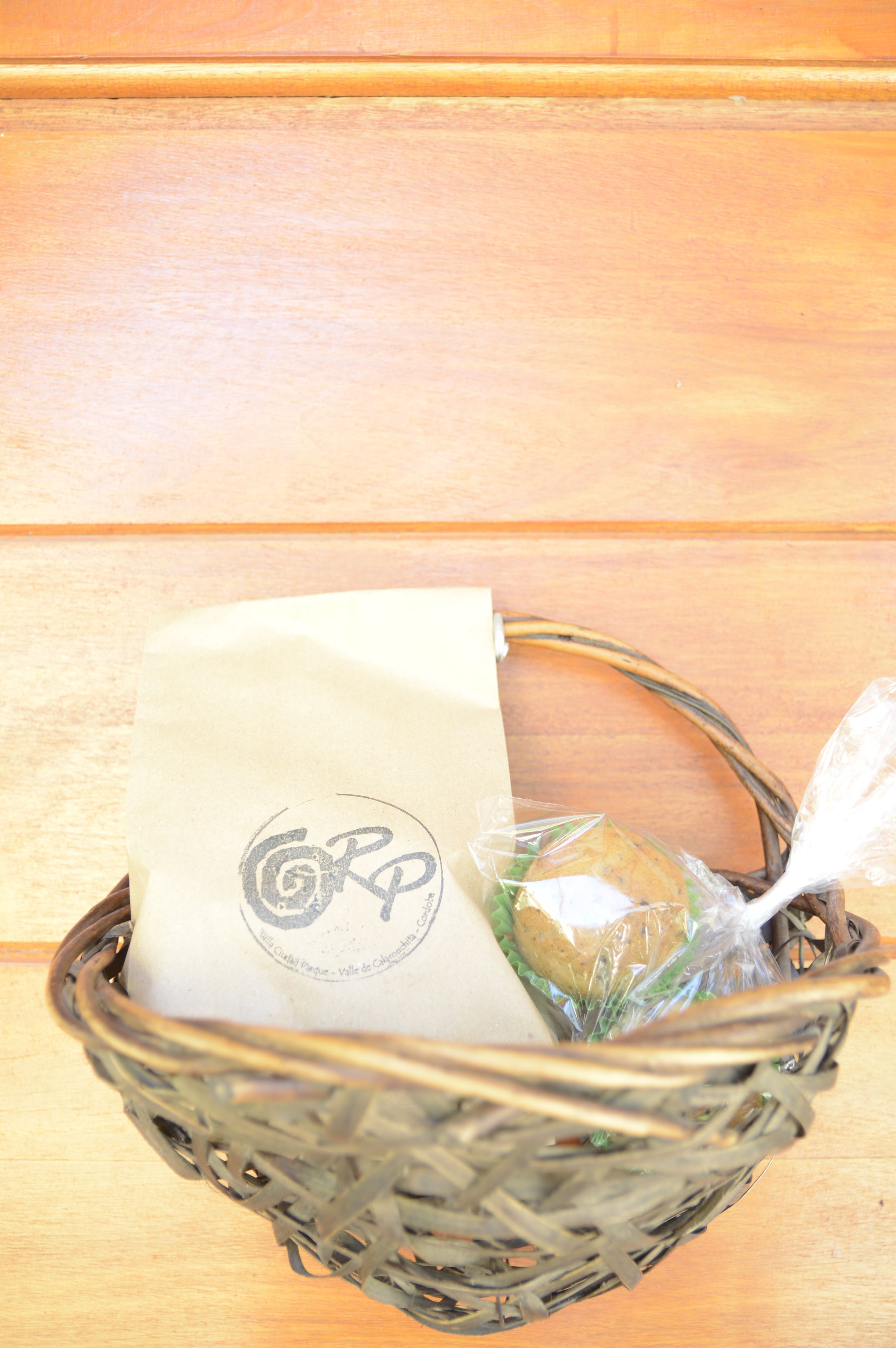 A wicker basket containing a white paper bag with a logo and a wrapped item.