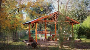 A wooden gazebo with benches, surrounded by trees and a grassy area.