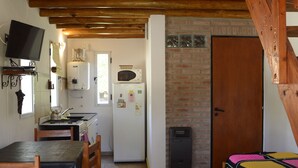 A compact kitchen with a dining area, a bed with a colorful blanket, and a wooden staircase.