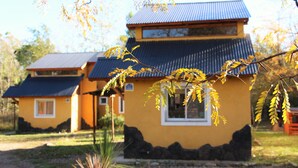 A yellow building with a blue roof, surrounded by a stone wall and a small garden.